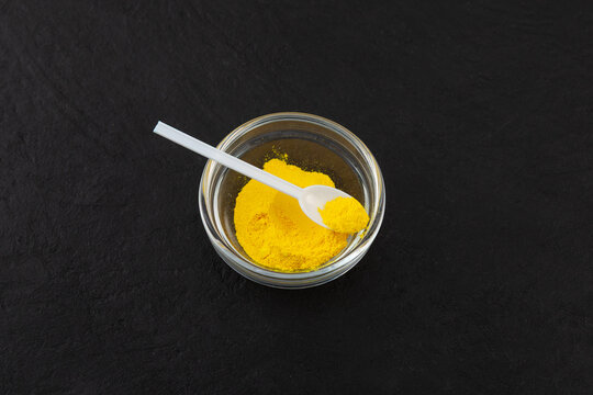 Quinoline Yellow dye, also known as Quinidine Yellow KT. Color index of 47005. Food additive E104 used in food and cosmetics industry. Golden yellow powder in glass bowl with measuring spoon