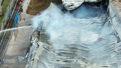 Drone view over a fiery industrial site where emergency crews spray water to contain a destructive...