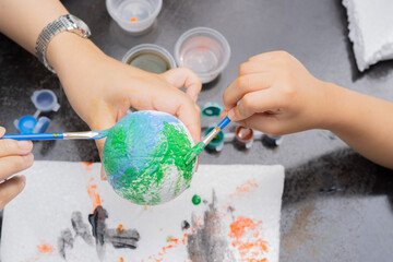 Mother and son's hands painting or coloring together on planet model on black table