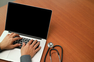 Doctor typing on laptop with stethoscope on wooden desk