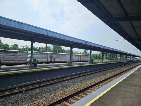 Wide-angle shot of an empty railway platform under a cloudy sky, showcasing parallel train tracks and a covered waiting area. Useful for transport, infrastructure, or travel visuals