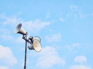 Upward shot of two public loudspeakers mounted on a pole with a blue sky background. Useful for...