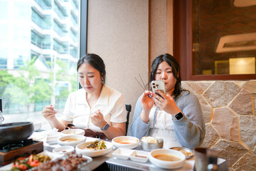 In a kalbi barbecue restaurant at a sunlit window table, two Korean women in their twenties in...