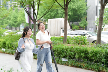 Two Korean women in their twenties in casual clothes walk along a boulevard sidewalk, talking and...