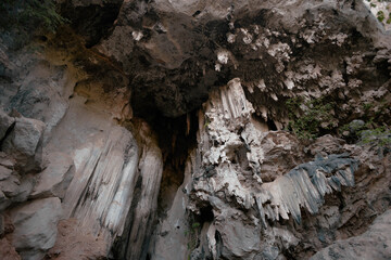 Intricate stalactites hang from the cave ceiling, while rugged rock formations rise from the ground in a natural setting highlighting geological beauty