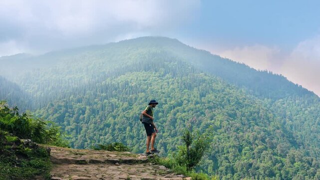 A man stands at the edge of a hill, gazing at the green mountains while trekking on the Buda Madmaheshwar Temple trail, Rudraprayag, Uttarakhand, India.