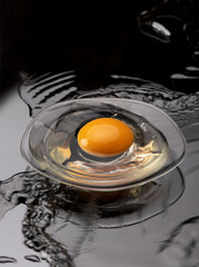 Single Egg Yolk in Glass Bowl on Reflective Black Surface, Fresh egg yolk in a glass bowl on a dark background.