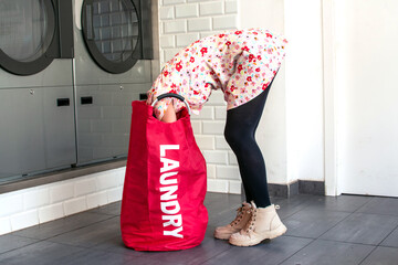 Woman picking up heavy laundry bag in laundromat