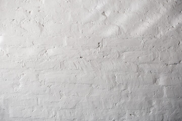 Play of light and shadow on a plastered wall. Textured white brick wall with uneven surface. Rough and grunge texture. Brick painted with white paint. Uneven, sloppy brickwork