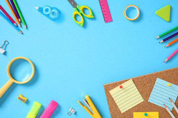 Frame of school supplies neatly arranged on blue background with sticky notes on corkboard....