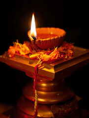 A lit diya oil lamp on an ornate stand with scattered flower petals and red thread