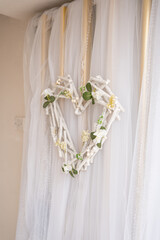 Decorative heart-shaped wreath made of twigs with small flowers hangs on a light fabric backdrop