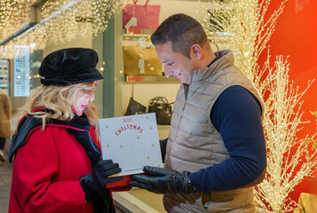 Couple sharing a Christmas gift near a festive store window