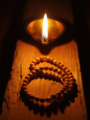 A lit diya lamp casting a warm glow on a wooden surface with prayer beads