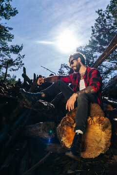 Man in plaid shirt and jeans sitting outdoors on log in sunlight