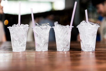 Four clear plastic glass filled with ice and pink straw on wood table.
