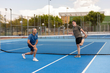 Friends stretching on outdoor tennis court before match