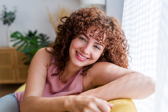 Portrait of smiling woman with curly hair relaxing indoors at home - Powered by Adobe