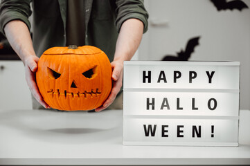 Closeup of spooky jack o lantern in man's hand with neon happy halloween sign. Festive banner