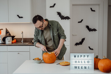 man carving jack o lantern in the kitchen, halloween concept 