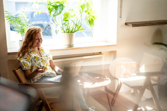 Woman with red hair working remotely on laptop in bright cafe