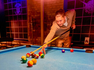Fototapeta premium Brunette middle-age man holding arm on billiard table, playing snooker game or preparing aiming to shoot pool balls. sport game snooker billiards