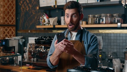 Shocked Caucasian barista man small business owner showing mobile phone display in cafeteria guy employer satisfied businessman say wow amazed male waiter demonstrating green screen chromakey app cafe