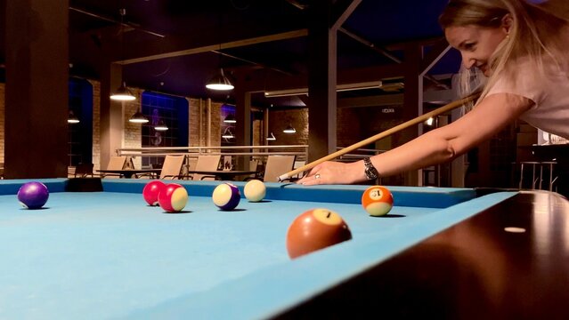 Middle-age blonde woman holding arm on billiard table, playing snooker game or preparing aiming to shoot pool balls. sport game snooker billiards
