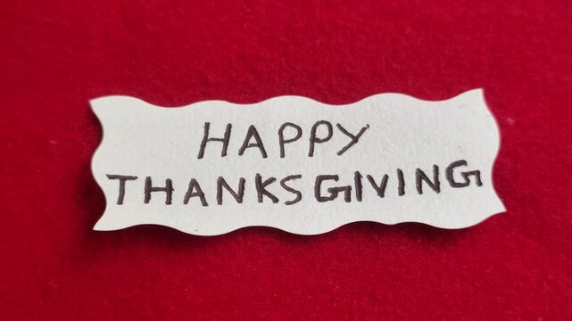 Happy Thanksgiving word letters text handwritten calligraphy design on white paper label note isolated on a red background surface with copy space. Closeup macro top view. Happy Thanksgiving concept.