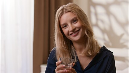 Happy healthy Caucasian lady drinking cup of mineral water refreshing morning in bedroom adult...