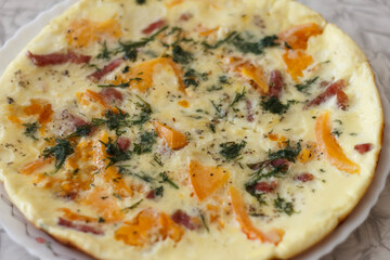 A close-up of a savory omelette with orange tomatoes, bell peppers, herbs, and pieces of ham