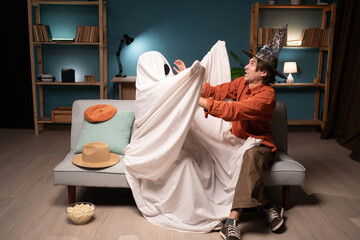 Man and unrecognizable person in ghost costume with black eyes having fun at home during Halloween...