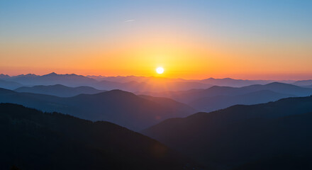 Obraz premium Golden sun rising over hazy blue mountain ranges, creating a serene dawn landscape