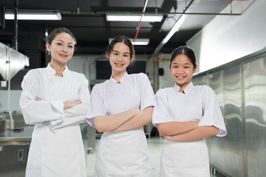 Restaurant kitchen. Group of female chef standing with crossed arms in kitchen, wearing white apron and smiling looking to camera - Powered by Adobe