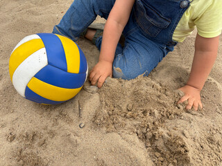 Child explores sand with hands next to volleyball. Outdoor sensory play for early childhood...
