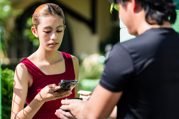 Young Southeast Asian woman pays for her takeaway food delivery by scanning a QR code using her smartphone at the gate