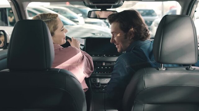 Young couple enjoying car dealership experience, discussing features while seated inside vehicle, showcasing excitement and connection in automotive purchase