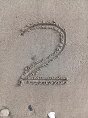 Number 2 drawn by hand in soft beach sand. A clean numeric sketch captured in a natural coastal environment.