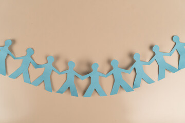 Blue paper cutout of people holding hands in a line on beige background. Symbol of unity, teamwork,...