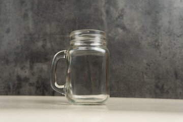 High-quality clear glass jar mug with handle placed on a neutral gray background. Ideal for product...