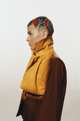 Woman with colorful shaved hairstyle wearing a shiny yellow jacket in profile, displaying edgy...