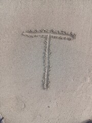 Close-up of the letter T written in smooth beach sand, featuring clean lines and natural texture.