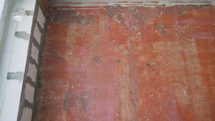 Red concrete floor showing signs of wear and tear next to white wall