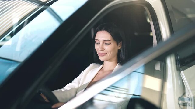 Confident woman sitting in a car at a dealership, showcasing her excitement for purchasing a new vehicle with bright interior lighting