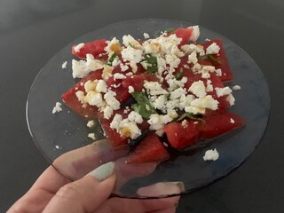 Closeup image of a woman holding a watermelon, feta and basil salad on a glass plate 
