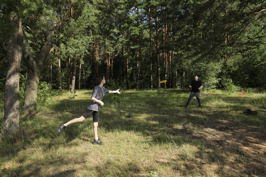 Two people playing catch in pine forest clearing, man and girl enjoying simple summer fun, family bonding and positive parenting in natural setting. - Powered by Adobe