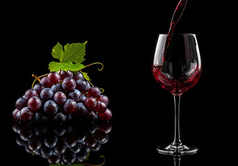 Red Wine Pours Beside Grapes on Black Reflective Surface
