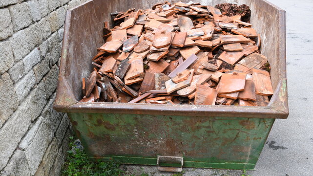 alte Biberschwanz Dachpfannen als Bauschutt in gr&uuml;nem Container