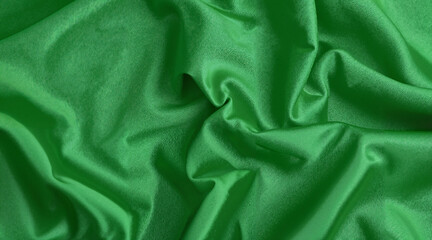 Green textured fabric draped in soft folds displaying shine  