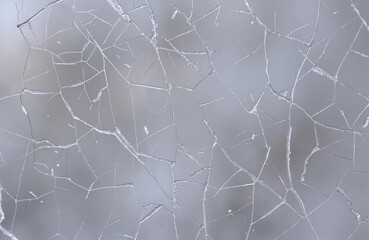 Ice cracks on window glass with blurred snowy background  